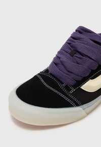 Baskets noires avec un dessus en daim texturé, dotées de lacets violets, de coutures blanches et d'une semelle en caoutchouc translucide.