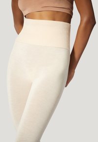 Leggings a vita alta in un morbido tessuto beige. Presentano una cintura larga con costine e una superficie liscia e elastica. Design aderente.
