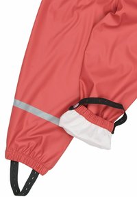 Jambe de pantalon imperméable rouge avec un ourlet élastique, bande argentée réfléchissante, et couvre-pied blanc ajustable avec sangle noire.