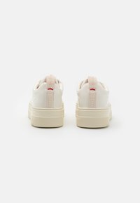 Zapatillas blancas con parte superior de cuero liso, suela de goma gruesa y tirador acolchado en el talón con logo en relieve en tonos rosa pálido y rojo.