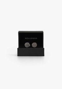 Gemelos de plata con diseño circular texturizado, que presentan la palabra grabada "SCALPERS", presentados en una caja de regalo negra texturizada.