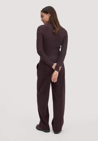 Donkerpaarse ribgebreide top met lange mouwen, gecombineerd met losse hoge taille broeken in dezelfde kleur. Model staat met de rug naar voren, handen achter de rug.