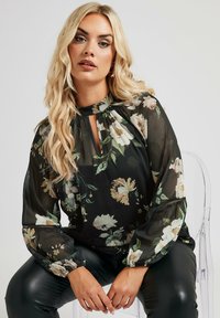 Blusa nera a fiori con maniche lunghe e trasparenti, scollatura a chiave e dettagli arricciati; presenta un leggero motivo floreale in crema e verde.