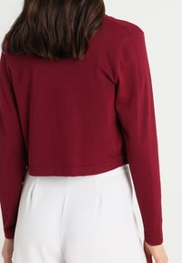 Cropped, long-sleeve cardigan in dark burgundy knit. Smooth texture with a simple design; clean hem and slight ribbing at cuffs.