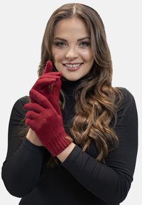 Czerwone, dziane rękawiczki z prążkowanymi mankietami, teksturowanym materiałem oraz małym logo na nadgarstku. Model pokazuje gest ręką.