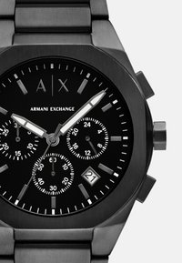 Reloj cronógrafo de acero inoxidable negro con una esfera de múltiples diales, acentos plateados, indicador de fecha a las 6 en punto y un acabado pulido.