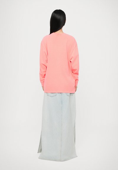 Long-sleeve pink sweatshirt, relaxed fit, cotton material. Paired with light blue denim skirt, floor-length, side slits, and back pockets.