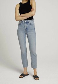 Högmidjade ljusblå jeans med rak ben, blekt tvätt och rå nederkant, kombinerat med en svart ribbad linne och svarta slidande sandaler.