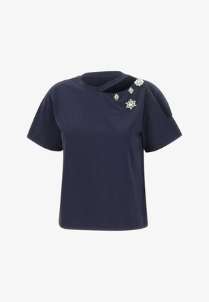 Top blu navy a maniche corte con scollo ritagliato e quattro spille decorative argentate con gioielli sulla spalla sinistra.