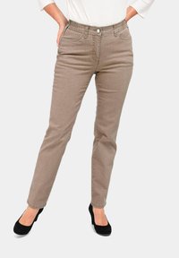 Hellbraune Jeans aus Denim mit tailliertem Schnitt, Fünf-Taschen-Design und einem Bund mit einem Metallknopf, kombiniert mit schwarzen Absätzen.