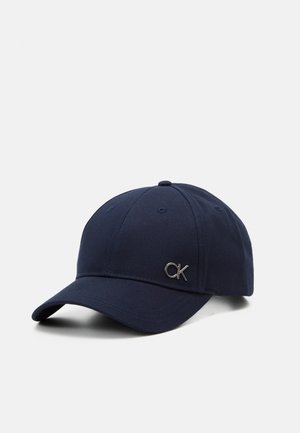 Casquette de baseball bleu marine avec visière courbée et logo métallique "CK" sur le devant, confectionnée en tissu avec un design de panneaux cousus.
