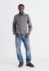 Black and white checked button-up shirt and blue jeans, with smooth texture and relaxed fit. Brown shoes complete the outfit.