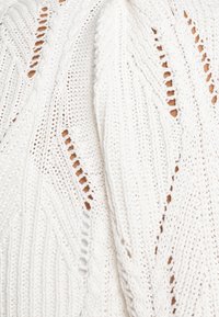 Biały sweter z dzianiny o misternych wzorach, pionowych prążkach i otwartych dzianinowych sekcjach. Miękka tekstura z luźnym, oversize'owym krojem.