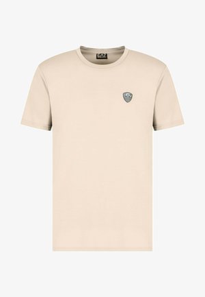 T-shirt in cotone beige con maniche corte, scollo rotondo e un piccolo logo ricamato in bianco e nero sul petto.