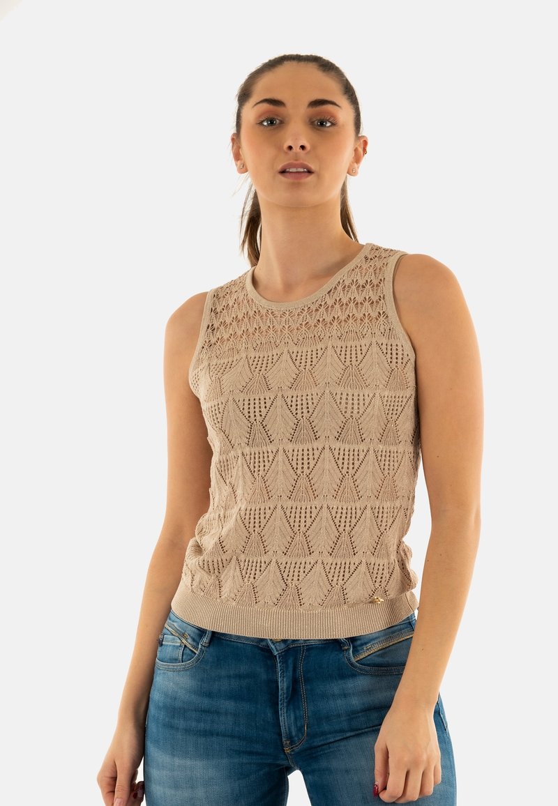 Top sin mangas de punto beige con un patrón geométrico texturizado, escote redondo y un dobladillo acanalado sutil, combinado con jeans de mezclilla azul.