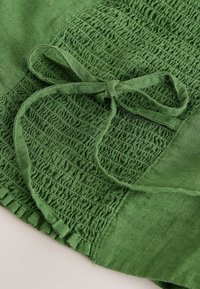 Tela verde con fruncido elástico recogido y detalle de lazo atado sobre un material suave y texturizado.