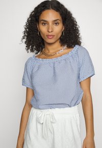 Blusa às riscas azuis e brancas com mangas curtas, um decote franzido e um corte relaxado, combinada com uma saia branca texturizada.
