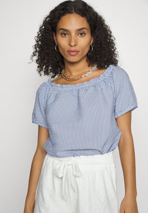 Blusa às riscas azuis e brancas com mangas curtas, um decote franzido e um corte relaxado, combinada com uma saia branca texturizada.
