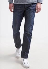 Mörkblå denimjeans med rak passform och klassisk femfickdesign. Bärs med vita låga sneakers.