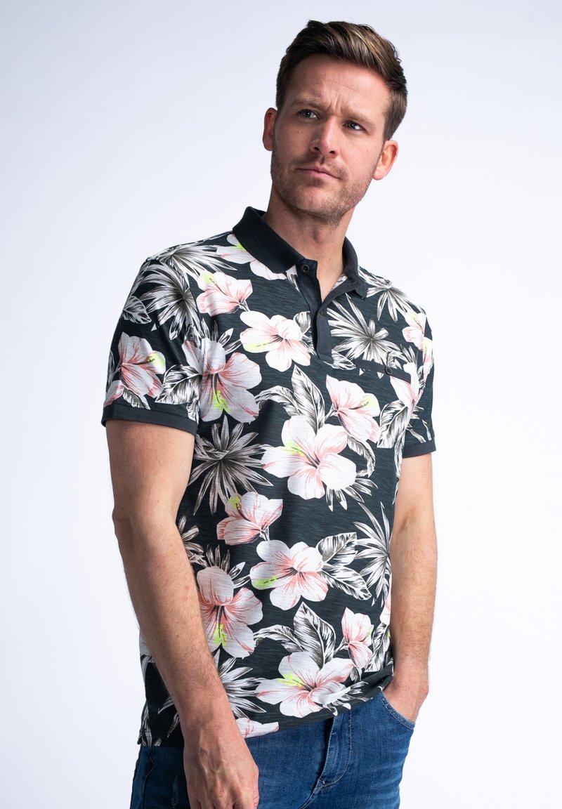 Polo de manga corta con un fondo oscuro, grandes patrones florales en rosa y blanco, cuello negro y una textura sutil.