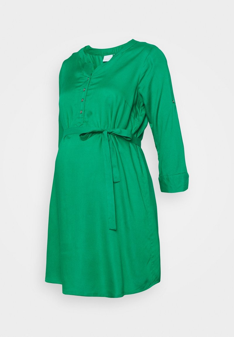 Robe de maternité verte mi-genou avec manches trois-quarts, encolure boutonnée et ceinture à nouer à la taille sur fond blanc.