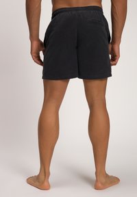 Pantaloni neri da uomo con un elastico in vita e una tasca sul retro. Il tessuto è liscio, con una vestibilità casual e senza motivi visibili.