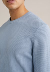 Svetlomodra teksturirana majica s kratkimi rokavi in okrolim izrezom, ki ima šahast vzorec in mehak finiš, kar poudarja njeno zračno tkanino.