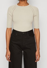 Light beige ribbed knit top with short sleeves and a round neck, paired with high-waisted black denim trousers.