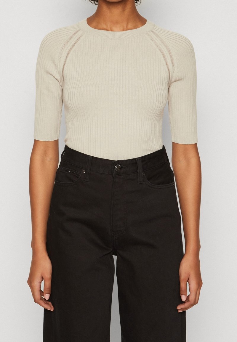 Light beige ribbed knit top with short sleeves and a round neck, paired with high-waisted black denim trousers.