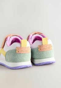 Baskets blanches avec des accents pastel en vert, jaune et rose. Elles présentent un talon texturé, une sangle Velcro et une semelle violette.