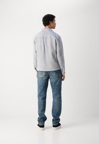 Stripet blå og hvit cordfløyelskjorte med spiss krage, knappestolpe foran og lange ermer, sammen med lyseblå denimjeans og svarte sko.
