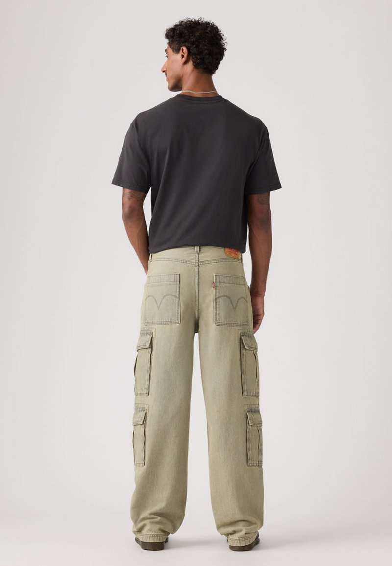 Schwarzes T-Shirt mit Rundhalsausschnitt und hellgrüne Cargo-Hose mit mehreren Taschen und verwaschenem Finish, von hinten gesehen.