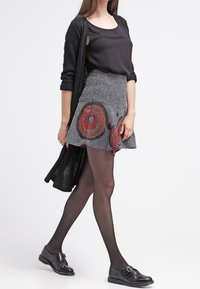 Un haut noir, un cardigan en tricot noir, une jupe courte à motifs avec des cercles rouges, des collants noirs et des chaussures noires avec un détail de boucle.