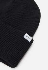 Svart strikket lue med ribbestruktur, med en hvit etikett som har "LES DEUX." Designet er enkelt og sitter tett.