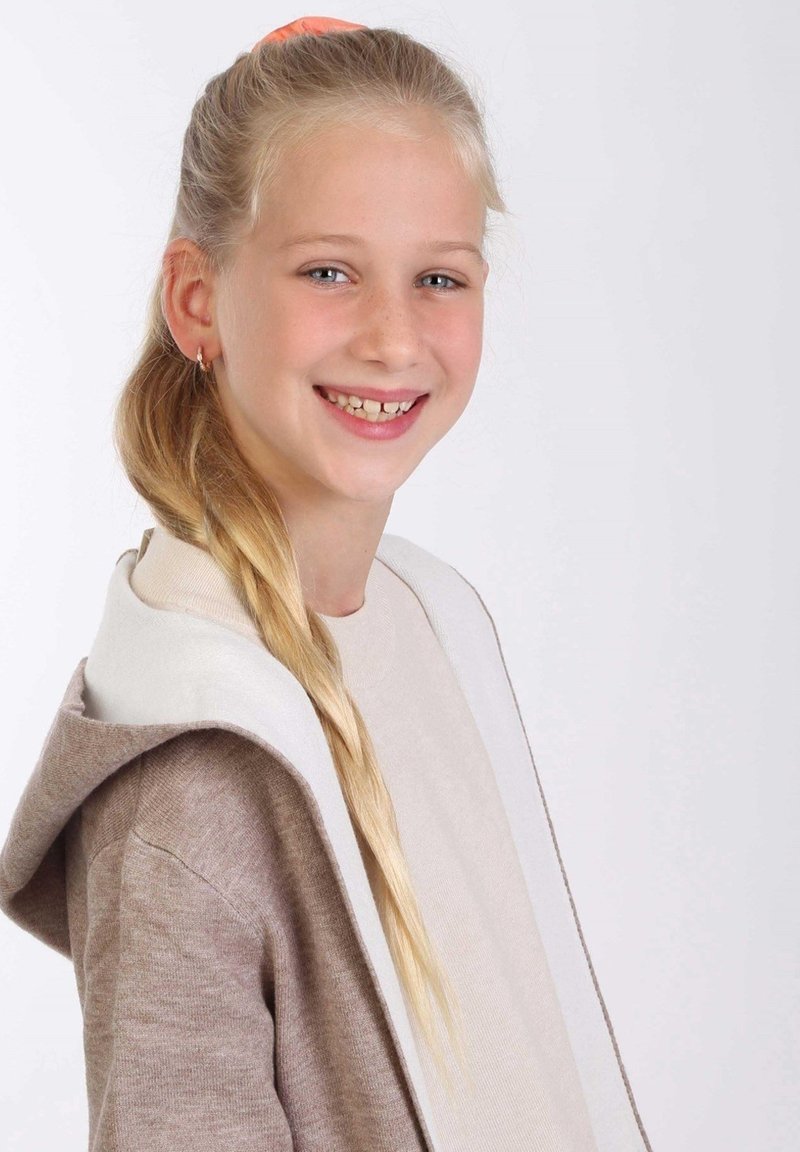 Beige en bruine gebreide hoodie met een witte voering, voorzien van een grote capuchon en een soepele textuur, gedragen over een lichtgekleurde top.