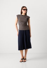 Hnědo-beige pruhovaný top s krátkým rukávem, kombinovaný s plisovanou tmavě modrou sukní a hnědými sandály. Minimalistický design.