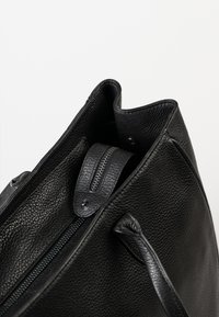 Zwarte leren handtas met een gestructureerde textuur, een ritssluiting en twee stevige handvatten met een gladde afwerking.