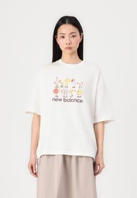 Balta medvilninė marškinėliai su per dideliu siluetu, su spalvinga grafika, kurioje pavaizduoti žaismingi personažai ir apačioje užrašas "new balance".