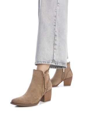 Botines de ante en tono beige con punta afilada, cremallera lateral y tacón apilado; combinados con pantalones de mezclilla gris cortos.