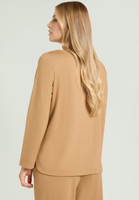 Camiseta de manga larga Tan con un sencillo cuello redondo, confeccionada en tela suave. Vista trasera que muestra una textura lisa y un diseño de corte recto.