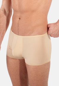 Shorts sportivi beige realizzati in tessuto liscio e elasticizzato. Presentano un design aderente e cuciture a contrasto. Adatti per l'uso attivo.