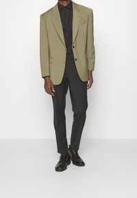 Oliwkowa marynarka z klapami, zestawiona z czarną koszulą i czarnymi spodniami. Strój uzupełniają czarne buty eleganckie i schludna sylwetka.