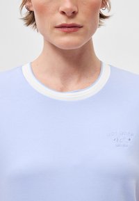 Απαλή μπλε μπλούζα με λευκό ριμπ γιακά. Κεντημένο λογότυπο στο στήθος. Μαλακό υλικό με λεία υφή.