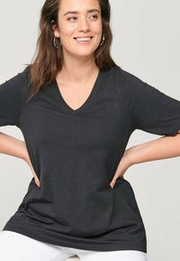 Czarna koszulka V-neck z miękkiego materiału, o luźnym kroju i krótkich rękawach, z gładką teksturą i minimalnymi detalami.