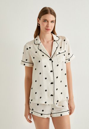 Conjunto de pijama de manga corta en blanco con lunares negros. Presenta ribete negro, un bolsillo en el pecho y cierre frontal de botones. Textura de tela suave.