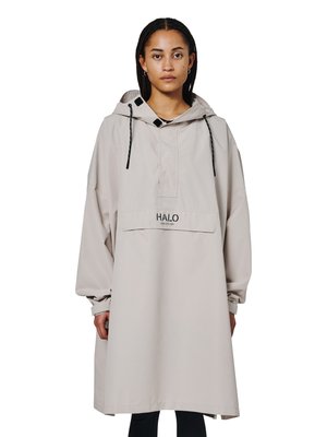 Kvinde med flettet hår iført en løs beige hættetrøje med frontlomme mærket "HALO" og sorte snore.