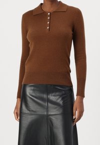 Maglione lavorato a maglia marrone con scollo a colletto, piastra a cinque bottoni e maniche lunghe; abbinato a una gonna in pelle nera.