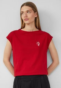 Rode katoen t-shirt met omgeslagen mouwen, voorzien van een kleine witte schelpgrafiek op het linker borstgebied. Eenvoudige ronde halslijn, ontspannen pasvorm.