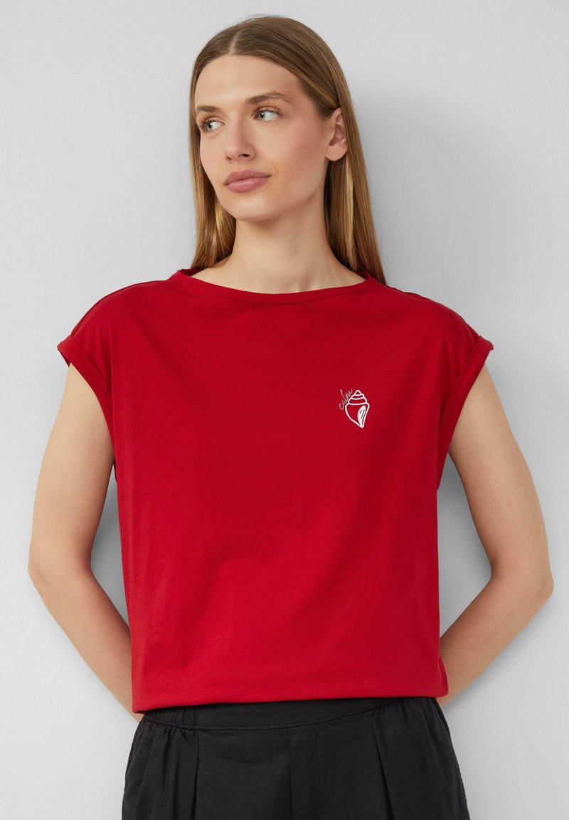 Rode katoen t-shirt met omgeslagen mouwen, voorzien van een kleine witte schelpgrafiek op het linker borstgebied. Eenvoudige ronde halslijn, ontspannen pasvorm.