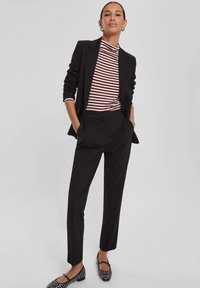 Blazer nero su una maglietta aderente a strisce bordeaux e bianche, abbinato a pantaloni neri e ballerine a pois.
